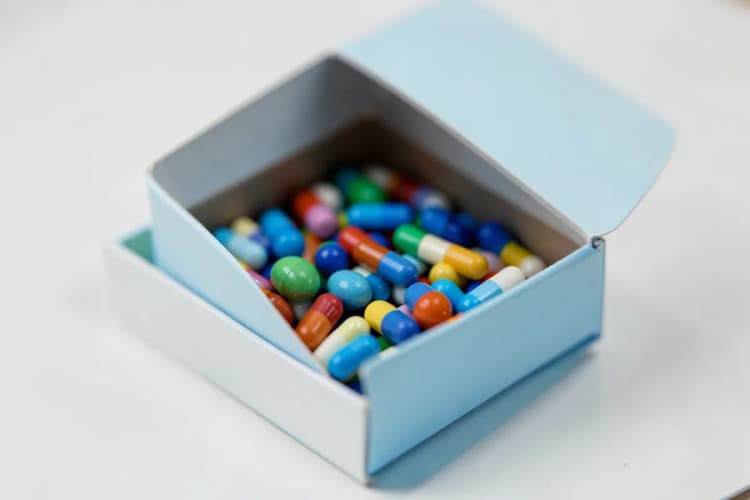 Uma caixa de comprimidos aberta com algumas pílulas coloridas visíveis.