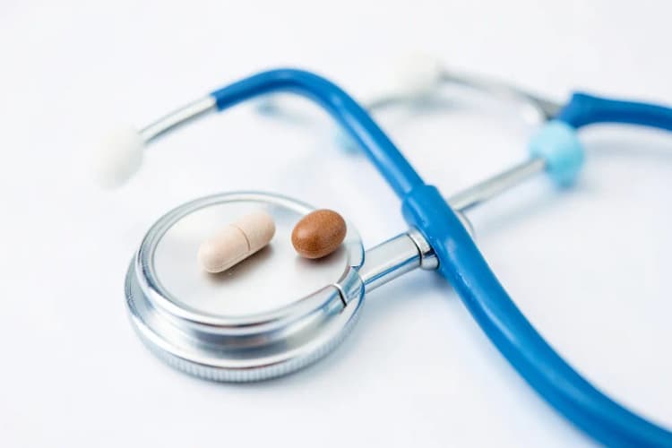 Uma pílula médica e um estetoscópio sobre um fundo branco.