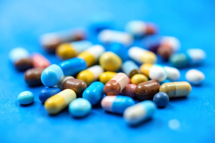 Comprimidos e cápsulas coloridas espalhadas sobre um fundo azul, representando tratamentos para depressão.