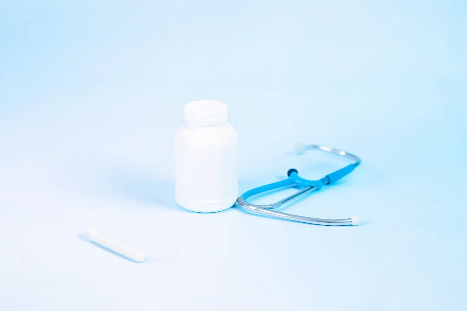 Um frasco de comprimidos de antidepressivos com um estetoscópio sobre um fundo branco e azul claro.
